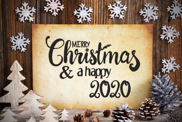 Fototapeta na wymiar Old Paper With English Text Merry Christmas And Happy 2020. Christmas Decoration Like Tree, Fir Cone And Snowflakes. Brown Wooden Background