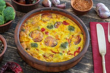 Ceramic bowl with vegetable frittata, simple vegetarian food. Frittata with egg, tomato, pepper, onion, broccoli and cheese on wooden table. Italian egg omelette