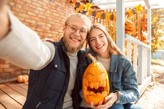 Halloween Preparaton Concept. Young couple sitting at porch with jack-o'-lantern taking selfie posing to camera happy