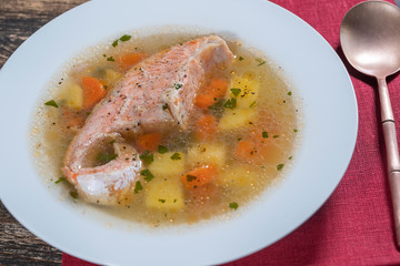 Fresh salmon fish soup with carrots and potatoes in a white plate, close up