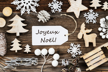 One White Label With French Text Joyeux Noel Means Merry Christmas. Frame Of Christmas Decoration Like Tree, Sled, Star And Fir Cone. Wooden Background