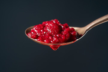 Thick red raspberry jam dripping from the spoon, one drop, on black background, close up