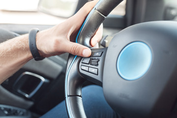 Young adult man adjusting car settings on steering wheel