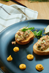 Salmon tartare on fried croutons served on a stylish black plate. Restaurant Food. Wooden bakcground. Close up