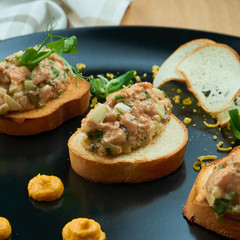 Salmon tartare on fried croutons served on a stylish black plate. Restaurant Food. Wooden bakcground. Close up