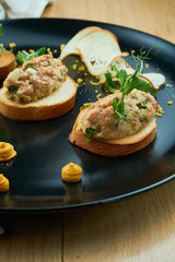 Salmon tartare on fried croutons served on a stylish black plate. Restaurant Food. Wooden bakcground. Close up