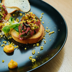 Beef tartare on fried croutons served on a stylish black plate. Restaurant Food. Wooden bakcground. Close up