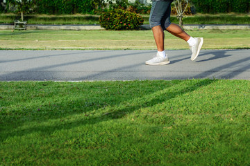 Side view of a jogger legs were running slowly on the asphalt road in the park with green grass...
