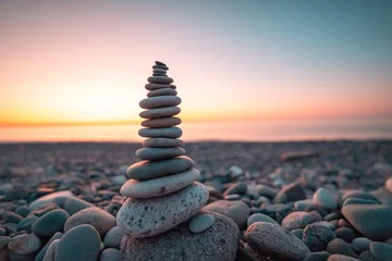 Fotobehang Zen Stone pyramid on the background of sunset and sea on pebble beach symbolizing stability, zen, harmony and balance  © Goffkein