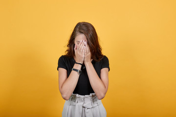 Cute and beautiful girl in black puts her hands in front of her face. She is indicating two expressions as she is shy to someone, or she is upset and wants to close er eyes forcefully.