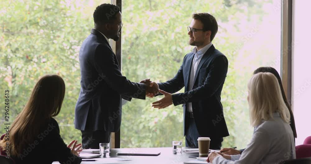 Sticker Proud african manager promoting handshaking caucasian employee at team meeting