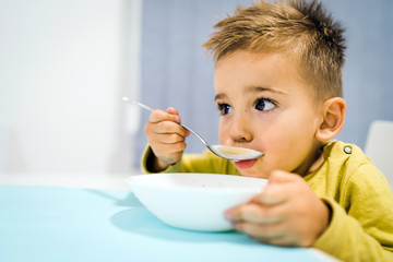 Portrait of small boy child eating soup meal or breakfast having lunch by the table at home with...