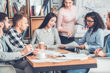Startupers working together at office sitting looking at documents thoughtful while pregnant woman...