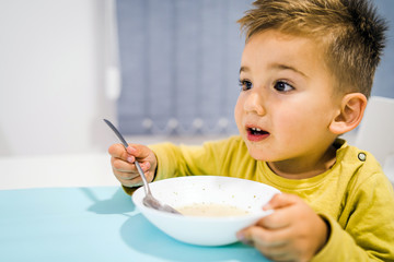 Portrait of small boy child eating soup meal or breakfast having lunch by the table at home with...