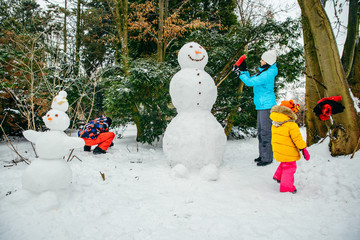 young family building snowman in snowed park. little toddler girl helping