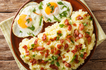 Tasty hot mashed potato with bacon and parsley served with fried eggs close-up on a plate. Horizontal top view