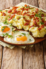 Spiced mashed potatoes with bacon and parsley served with fried eggs close-up on a plate. vertical