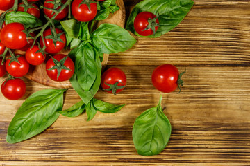 Fresh cherry tomatoes with green basil leaves on a wooden table. Top view