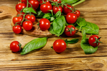 Fresh cherry tomatoes with green basil leaves on a wooden table