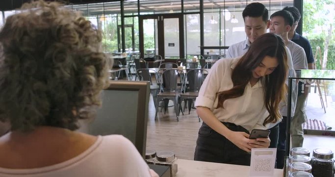 Customer in cafe makes payment with mobile phone while queue of customers wait to be served. 4K Mobile payment concept.
