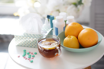 Cup of tea with lemon standing near plate with oranges and vitamins