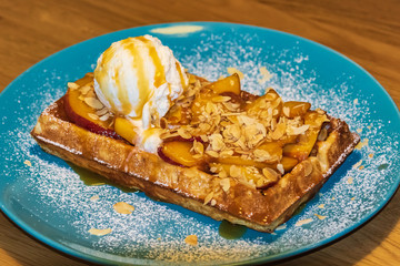 Belgian waffles with a scoop of white ice cream decorated with fruits and almonds. Powdered sugar on a blue plate. Close-up. Side view.