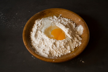 Chicken egg beaten into flour. Flour and chicken egg in a wooden plate on a gray background