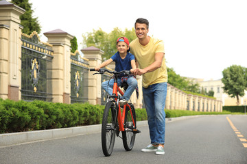 Obraz premium Dad teaching son to ride bicycle outdoors