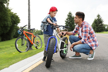 Fototapeta na wymiar Dad teaching son to ride bicycle outdoors