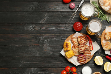 Flat lay composition with barbecued meat and vegetables on black wooden table. Space for text