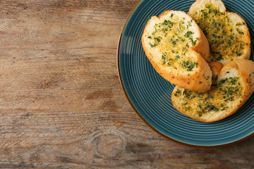 Slices of toasted bread with garlic, cheese and herbs on wooden table, top view. Space for text