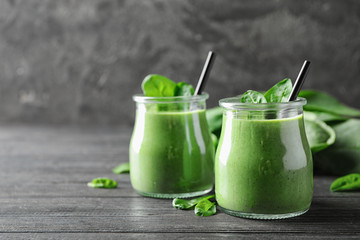 Jars of healthy green smoothie with fresh spinach on grey wooden table. Space for text