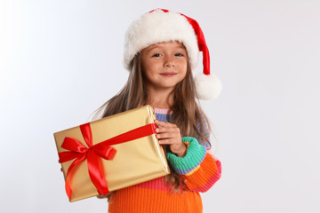 Happy little child in Santa hat with gift box on light grey background. Christmas celebration