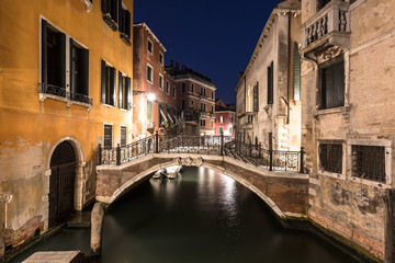 Fototapeta na wymiar Night view of a narrow canal with ancient buildings in Venice in Italy