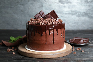 Freshly made delicious chocolate cake on black wooden table against grey background