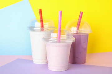 Different tasty milk shakes in plastic cups on color background