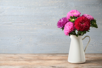 Jug with beautiful aster flowers on table against wooden background. Space for text