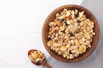 Bowl and spoon with healthy granola on white wooden table, flat lay. Space for text
