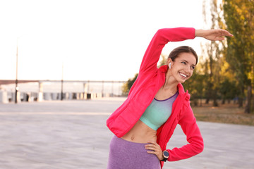 Young woman with wireless headphones listening to music while exercising outdoors. Space for text