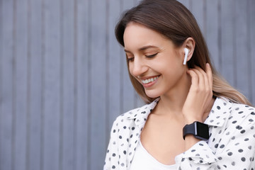 Young woman with wireless headphones listening to music near grey wall. Space for text