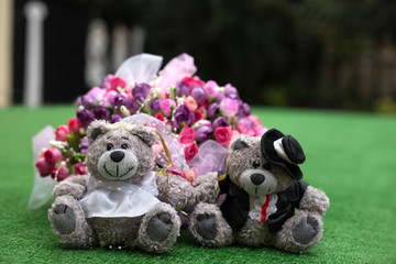 Wedding composition. Cute teddy bears couple on a green grass. Bouquet of flowers. Romantic card