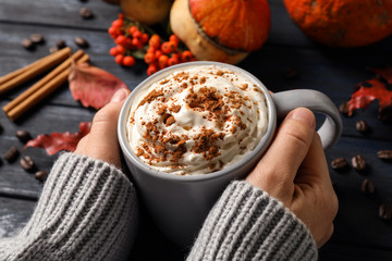 Woman with cup of tasty pumpkin spice latte at wooden table, closeup