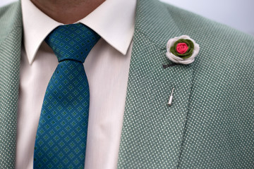 Man in green suit with blue tie and buttonhole closeup. Boutonniere with a red flower