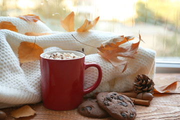 Composition with cup of hot drink, sweater and autumn leaves on windowsill. Cozy atmosphere