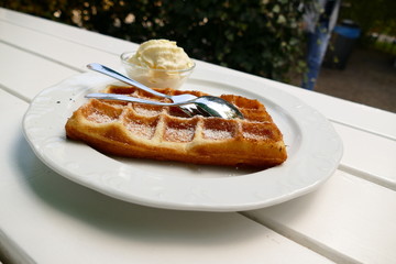 Frische Waffel mit Sahne und Puderzucker auf einem Teller im Garten