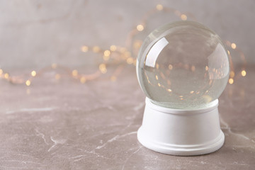 Snow globe on marble table against festive lights, space for text. Christmas season