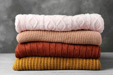 Stack of warm clothes on wooden table against grey background. Autumn season