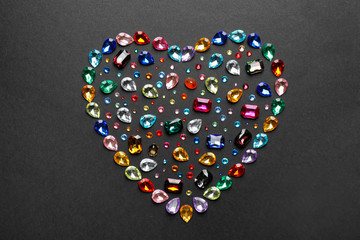 Heart shaped pile of different beautiful gemstones on black background, flat lay