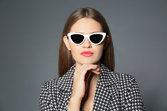 Young woman wearing stylish sunglasses on grey background