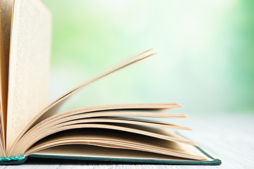 Naklejka premium Open book on white wooden table against blurred green background, closeup